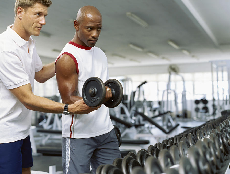 Coach helping a mid adult man exercise with dumbbells Photograph by Stockbyte