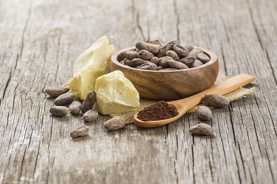 Cocoa butter or Cocoa bean solid oil with cacao powder in spoon and raw cocoa beans in wooden bowl on rustic backdrop, healthy natural oil Photograph by Mescioglu