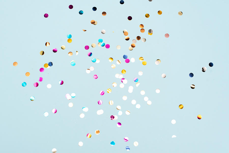 Colored confetti flying in the blue sky. Are small pieces or streamers of paper, mylar, or metallic material which are thrown at parades and celebrations. Photograph by Kseniya Ovchinnikova