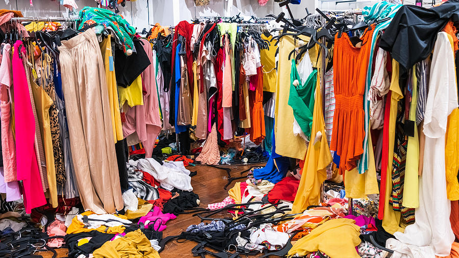 Colorful garments on racks and on the floor; fast fashion concept Photograph by Sundry Photography