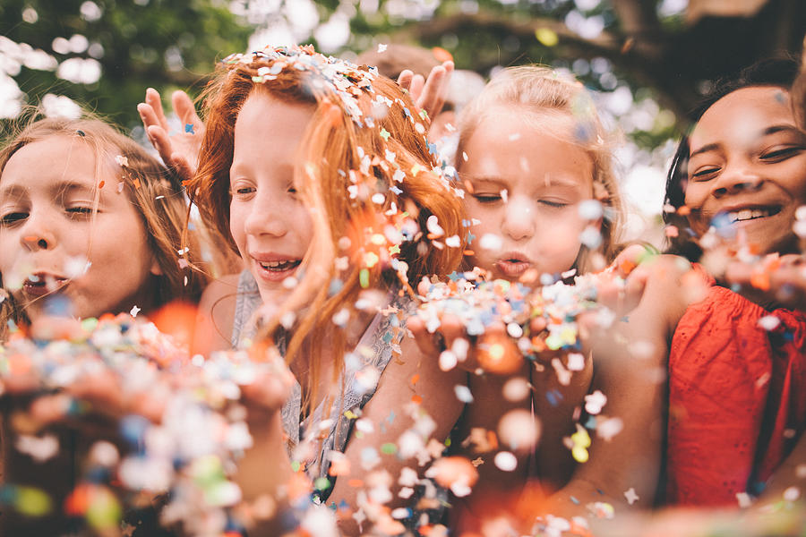 Colourful paper confetti being blown at the camera by children Photograph by Wundervisuals