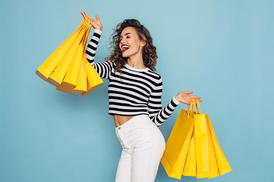 Conceptual photo of happy girl holds shopping packages on blue background Photograph by CoffeeAndMilk