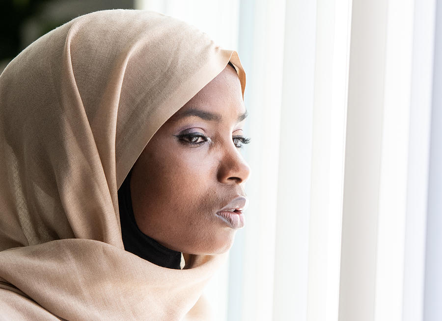Concerned black muslim woman looking through a window Photograph by Juanmonino