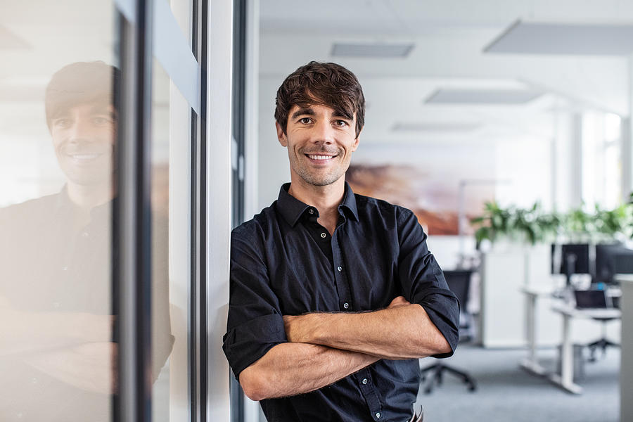 Confident businessman leaning on wall in creative office Photograph by Luis Alvarez