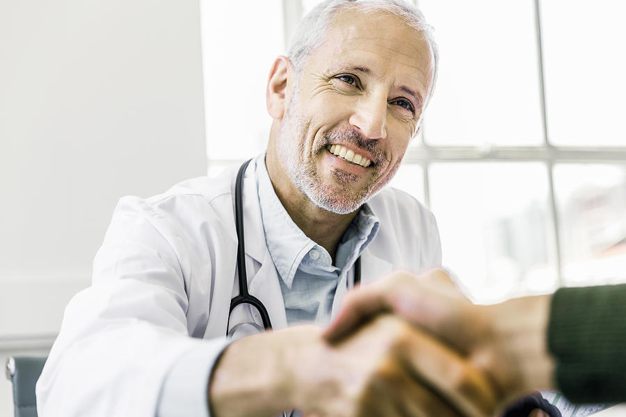 Confident doctor shaking hands with patient Photograph by Portra
