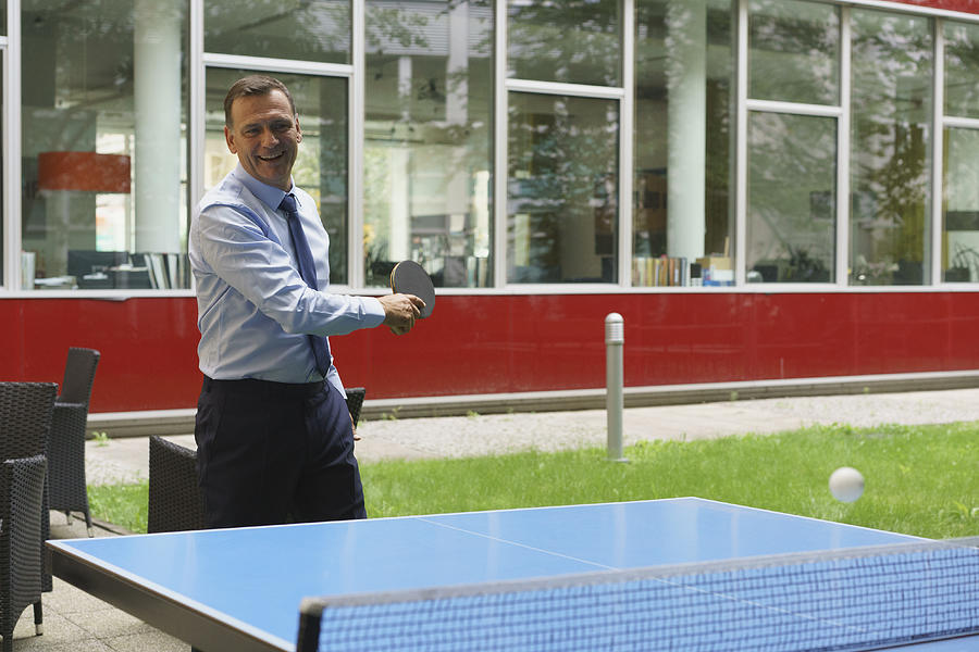 Confident happy businessman playing table tennis at creative office Photograph by Halfdark