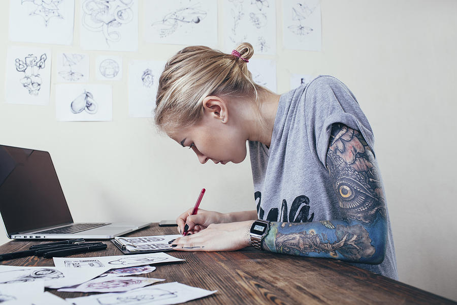 Confident tattoo artist working on designs by laptop at art studio Photograph by Vasily Pindyurin