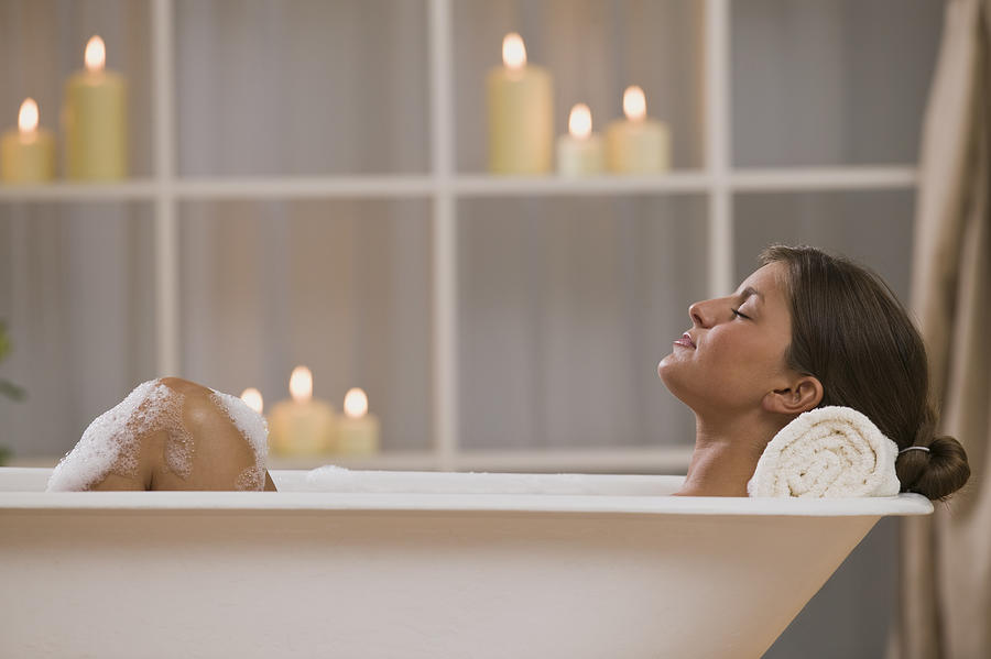 Content woman lying in bathtub with candles Photograph by Comstock Images