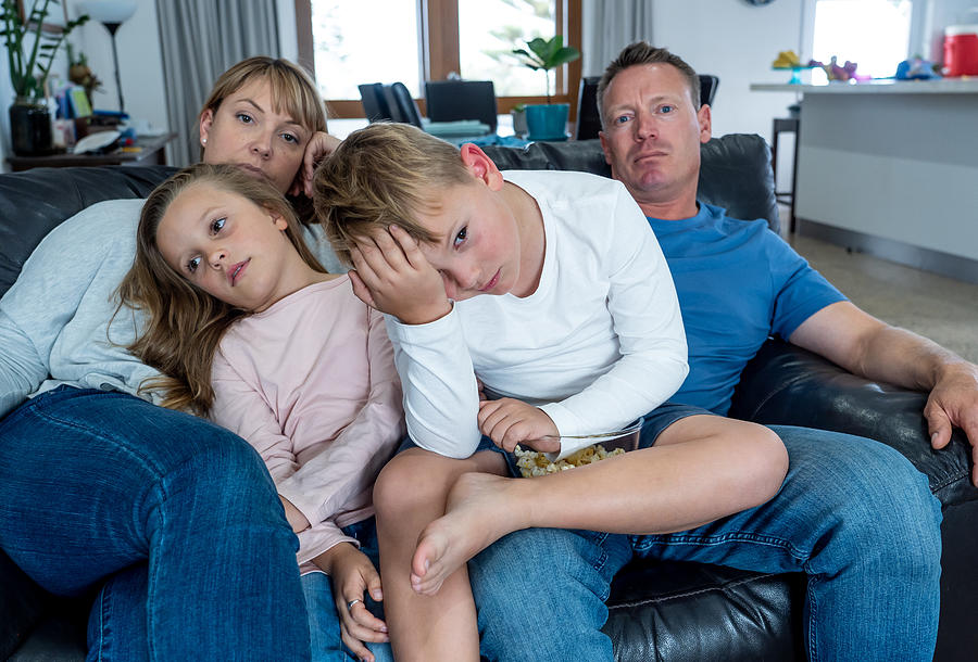 Coronavirus lockdow. Bored family watching tv helpless in isolation at home during quarantine COVID 19 Outbreak. Mandatory lockdowns and self isolation recommendations forces families stay home. Photograph by SB Arts Media