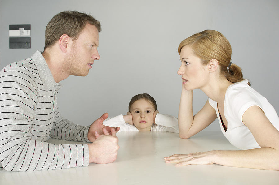 Couple arguing at table, girl in background covering ears with hands Photograph by Stock4b-rf