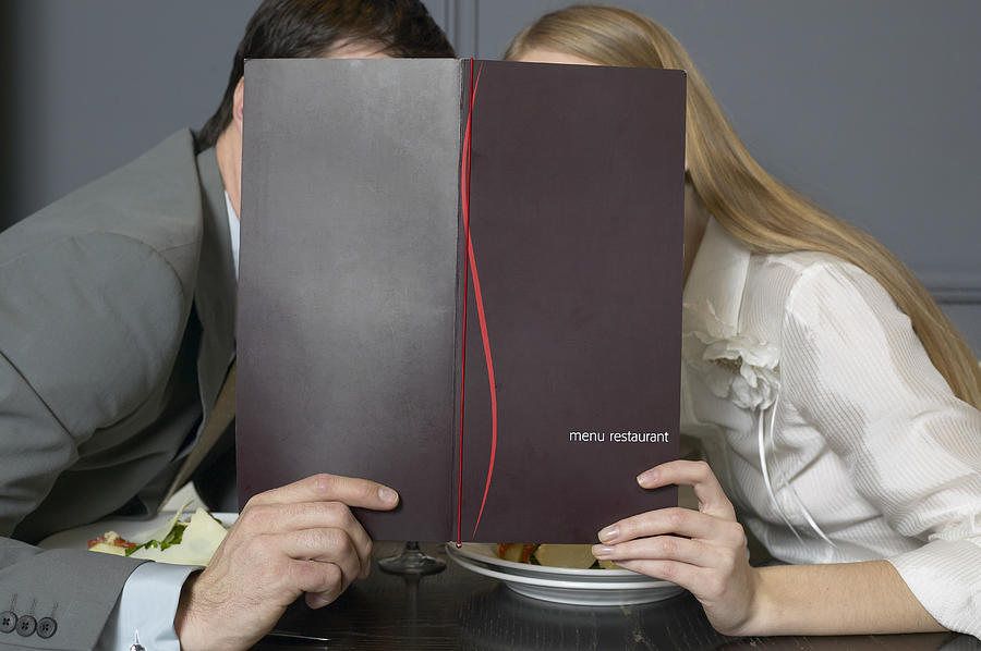 Couple at restaurant table leaning towards each other behind menu Photograph by Elke Hesser
