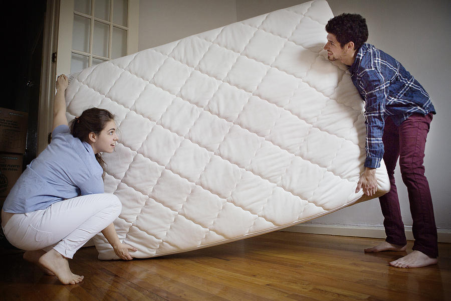 Couple carrying mattress in room Photograph by Cavan Images
