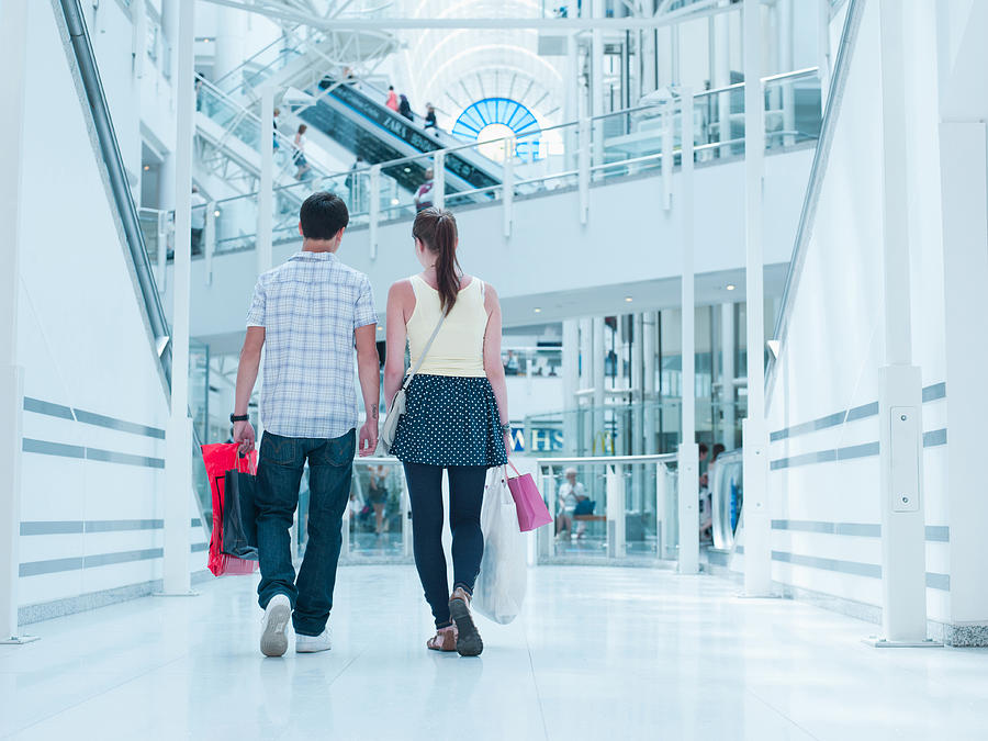 Couple carrying shopping bags in mall Photograph by Martin Barraud