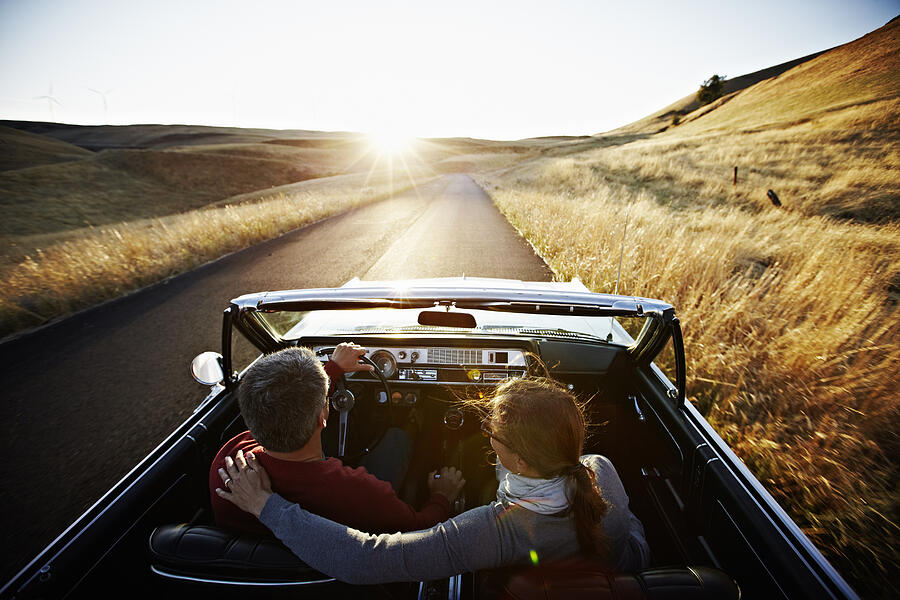 Couple driving convertible on empty road at sunset Photograph by Thomas Barwick