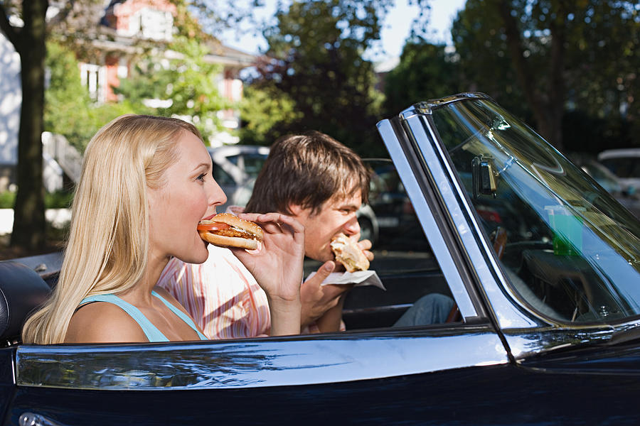 Couple eating burgers in convertible Photograph by Image Source