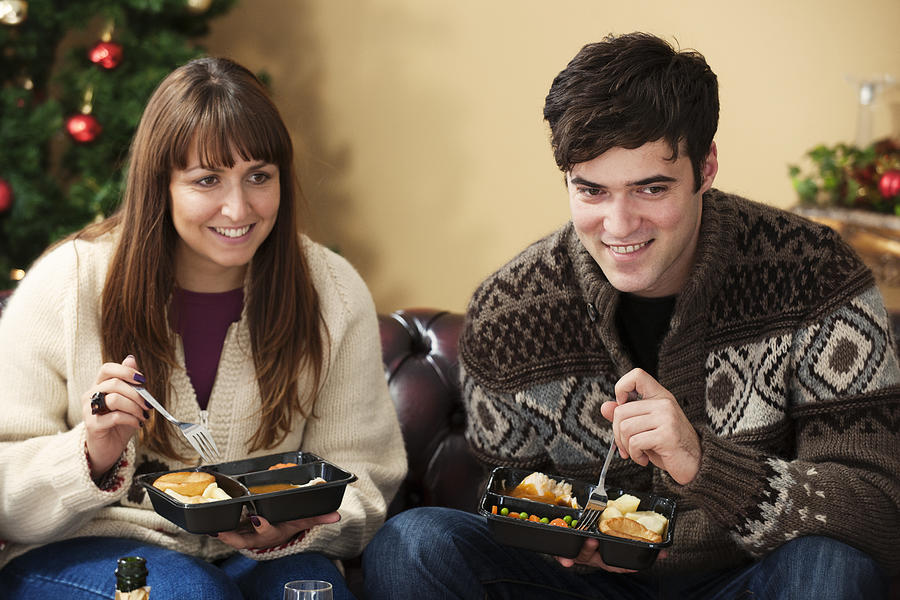Couple eating microwave dinners on sofa Photograph by Colin Hawkins