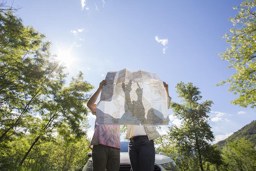 Couple examine road map near car, in forest Photograph by Ascent/PKS Media Inc.