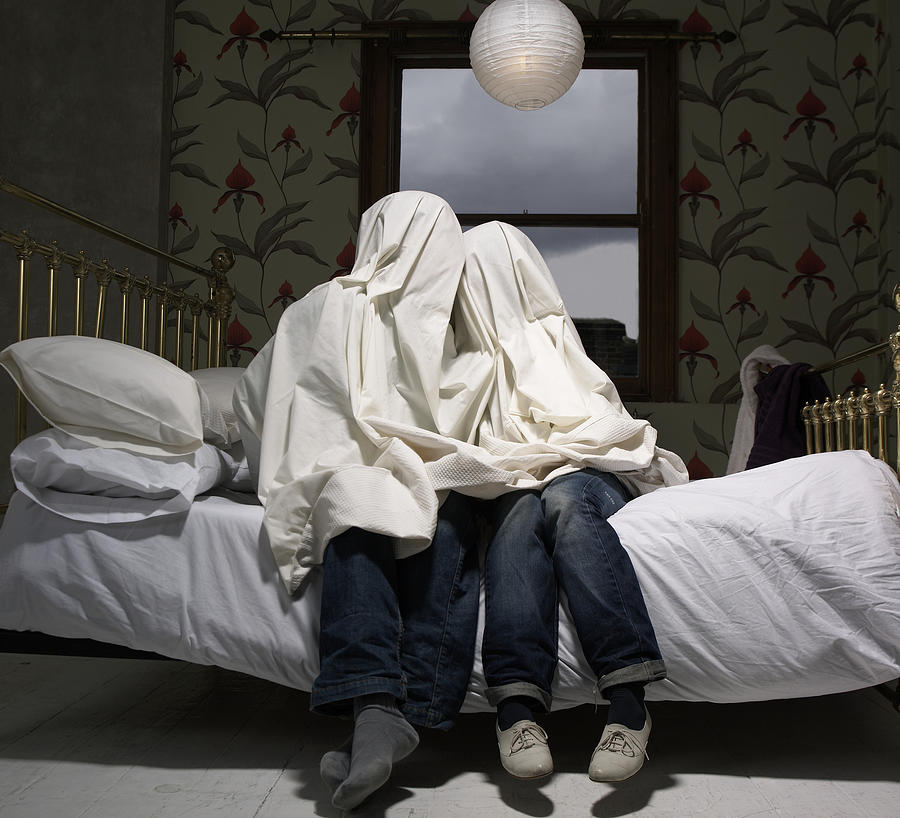 Couple hiding under sheet on bed Photograph by Simon Bremner