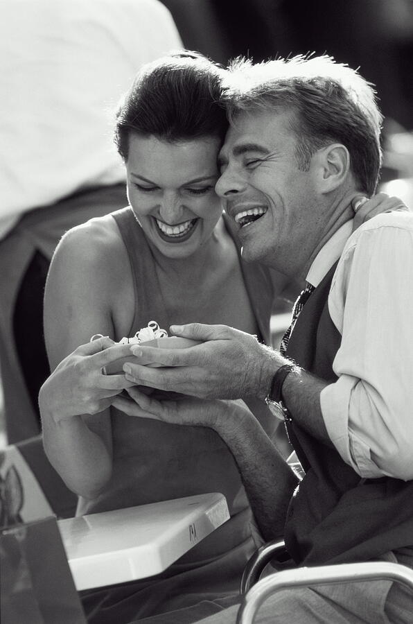 Couple holding present, laughing, sitting in outdoor cafe (B&W) Photograph by J.P. Nodier