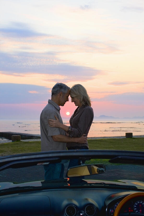 Couple hugging by convertible at sunset Photograph by Zero Creatives