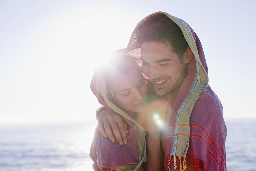 Couple hugging under blanket on beach Photograph by Hybrid Images