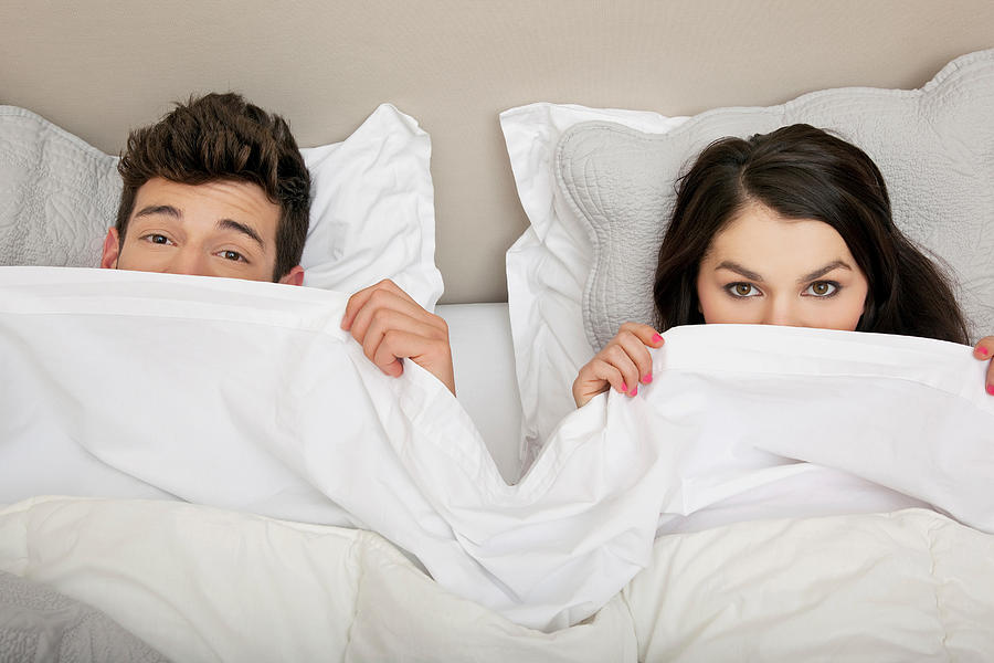 Couple in bed peeking behind duvet Photograph by Image Source