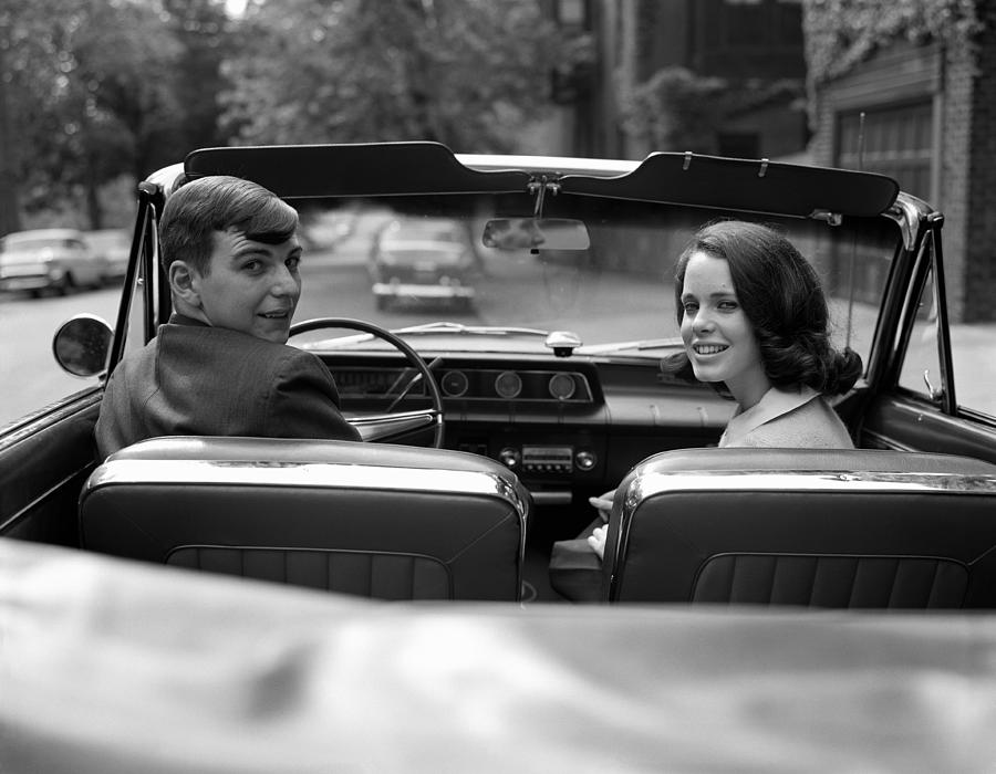 Couple in convertible, smiling, looking over shoulders, portrait. Photograph by H. Armstrong Roberts