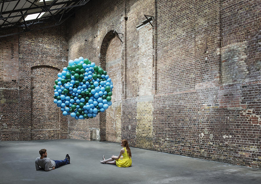 Couple in warehouse with globe made of balloons Photograph by Anthony Harvie