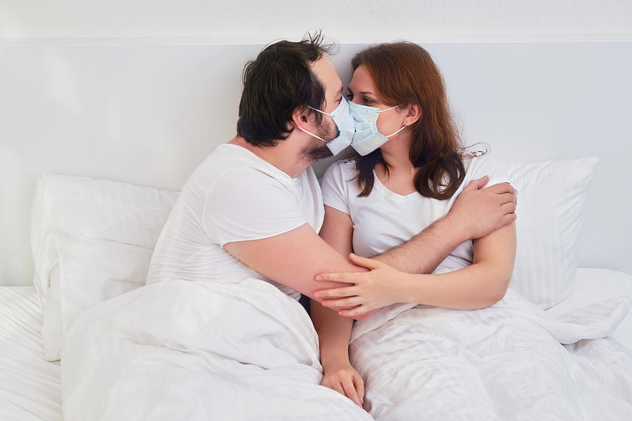 Couple kissing in bed in medical mask. Family relationships in isolation due to coronavirus. Photograph by Andrey Zhuravlev