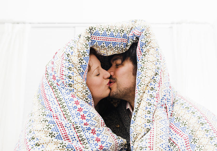 Couple kissing under duvet blanket Photograph by Redheadpictures