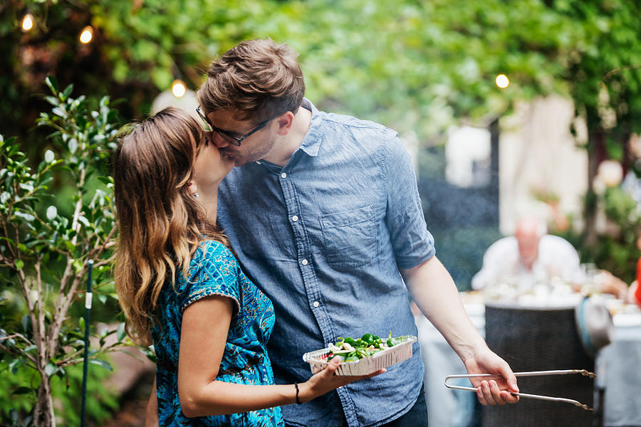Couple Kissing While Cooking At Family BBQ Photograph by Hinterhaus Productions