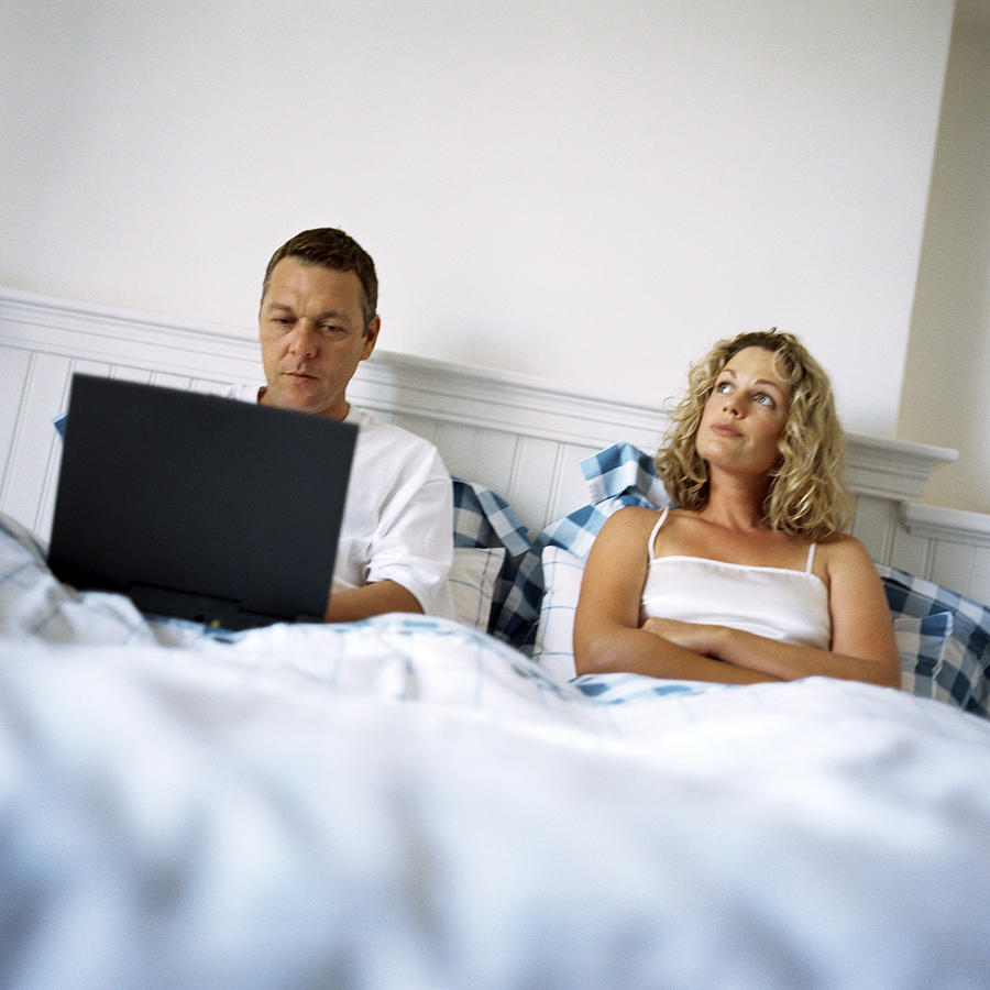 Couple laying in bed, man using laptop computer Photograph by Patrick Sheandell OCarroll