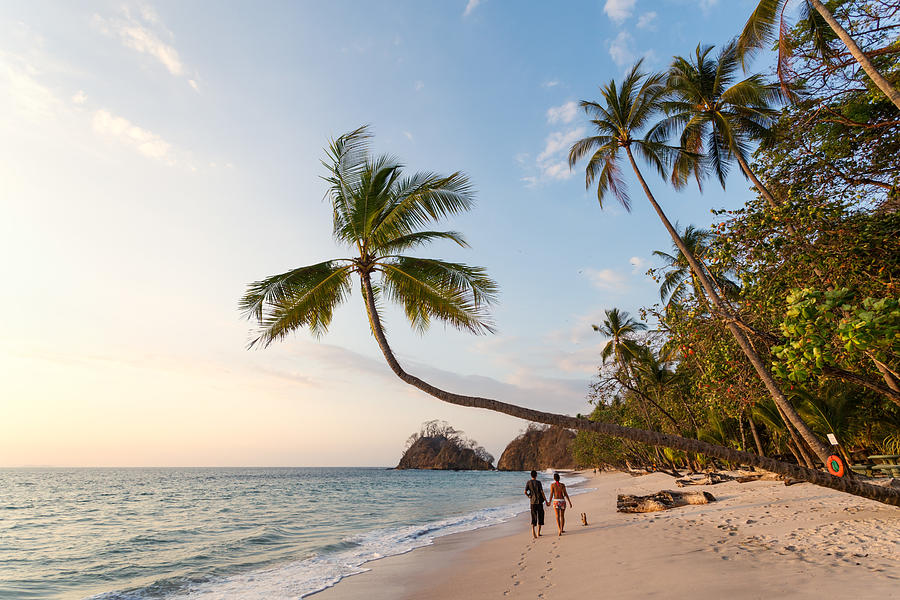 Couple of tourists walking on exotic beach at sunset, Costa Rica Photograph by Matteo Colombo