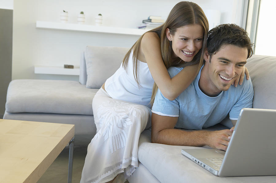 Couple on a Sofa in a Living Room Using a Laptop Computer Photograph by Flying Colours Ltd