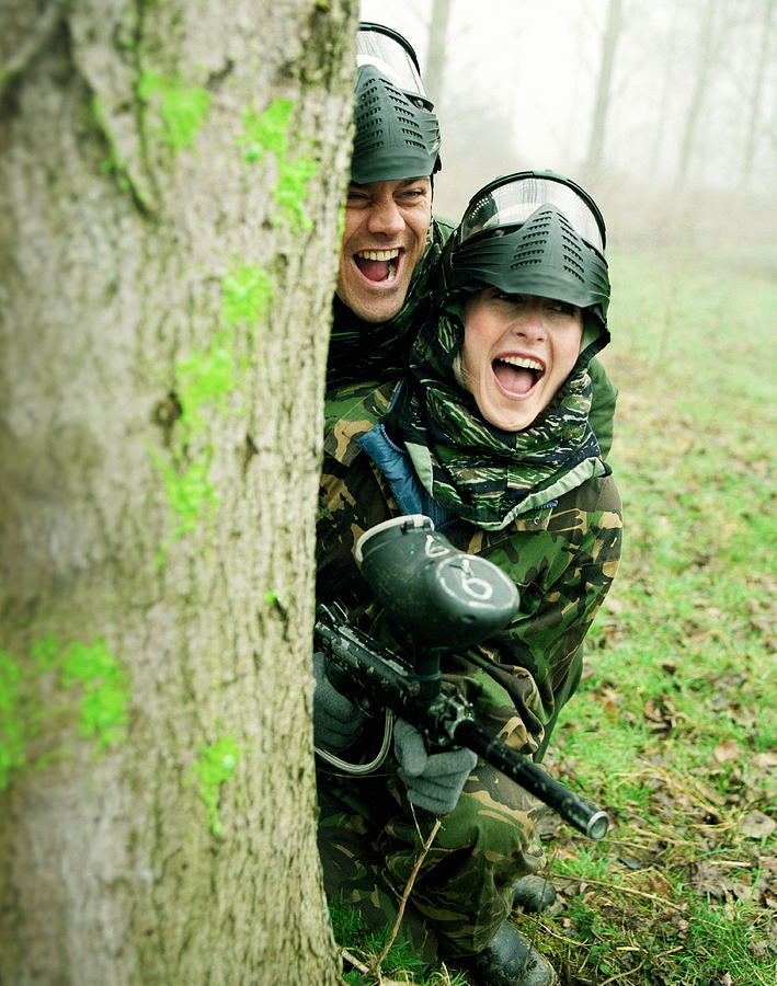 Couple paintballing, hiding behind tree Photograph by Alan Thornton