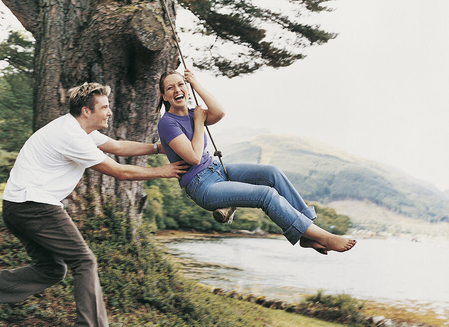Couple Playing on a Rope Swing, Man Pulling Woman Photograph by Digital Vision.