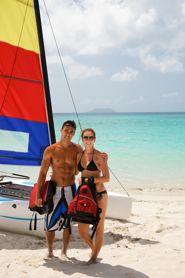 Couple Posing In Front Of Their Catamaran At A Beach Photograph by Cdwheatley