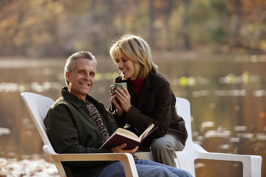 Couple relaxing by side of lake Photograph by Comstock