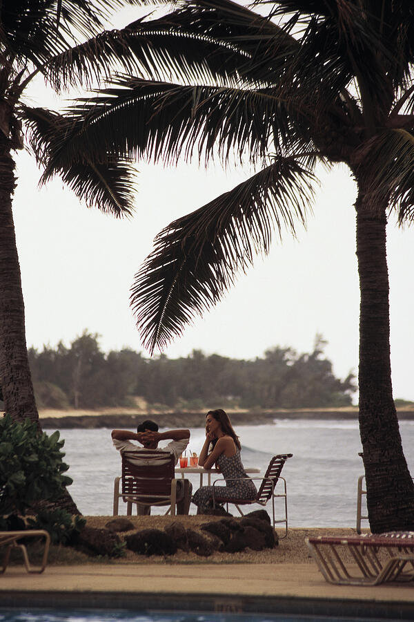 Couple relaxing under palm trees by the water Photograph by Comstock