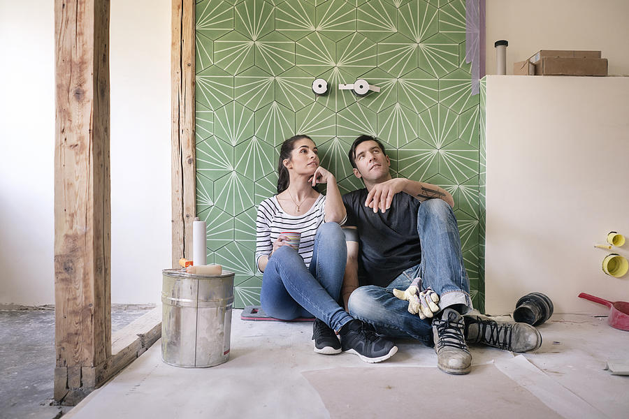 Couple renovating new house, sitting on ground planning bathroom Photograph by Westend61