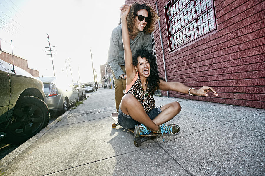 Couple riding skateboard on city street Photograph by Peter Griffith
