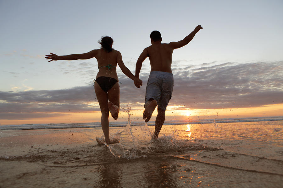 Couple runng into sea at sunset Photograph by Peter Cade
