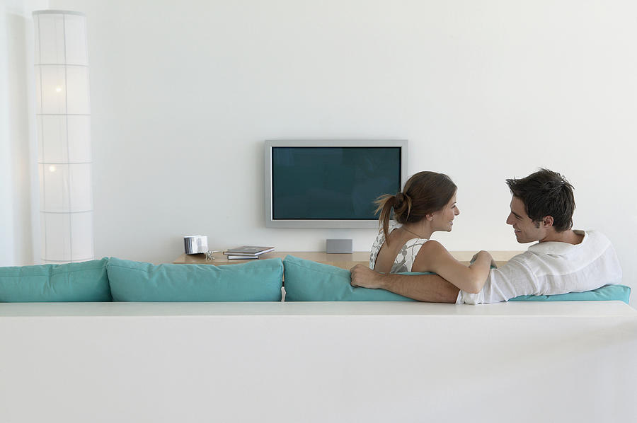 Couple Sits on Sofa Looking Face to Face, Plasma Television on Wall Photograph by Flying Colours Ltd