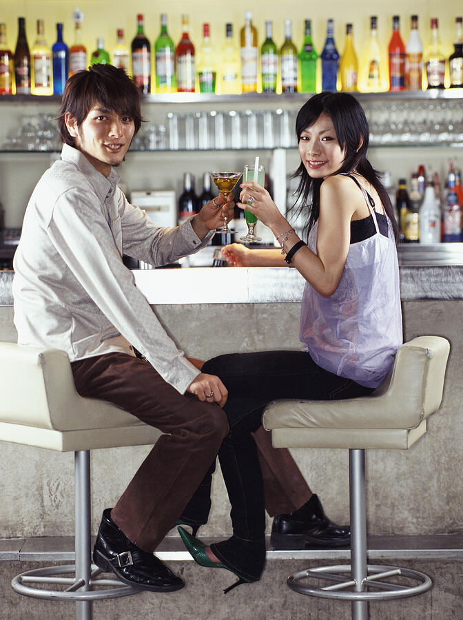 Couple Sitting at a bar Making a Toast With Cocktails Photograph by Digital Vision.