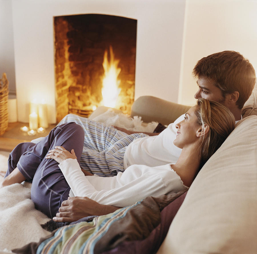Couple Sitting Close to Each Other on a Sofa by a Fireplace Photograph by Digital Vision.