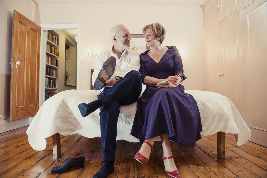 Couple sitting on bed, man putting on shoes Photograph by Redheadpictures