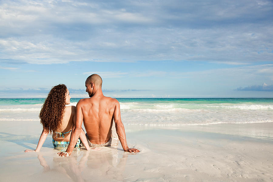 Couple sitting on sandy beach at waters edge Photograph by Image Source