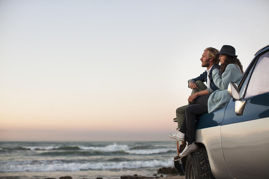 Couple sitting on truck looking at ocean view Photograph by David Lees