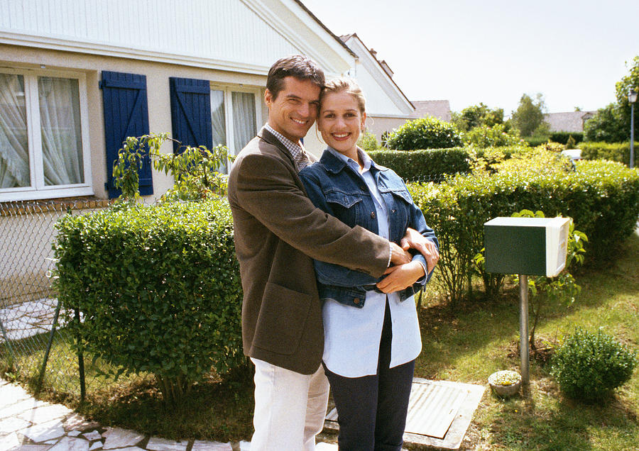 Couple standing in front of house, embracing Photograph by John Dowland
