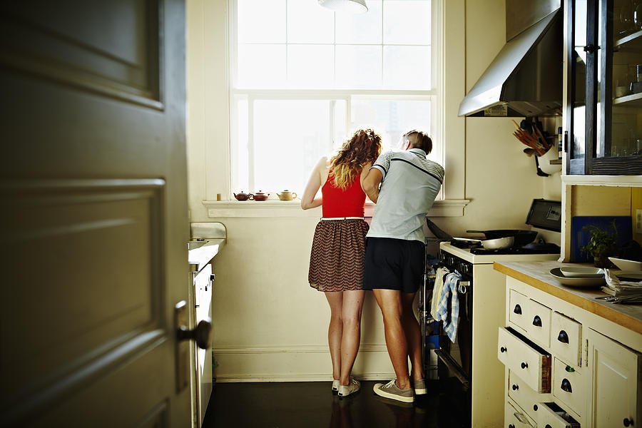 Couple standing looking out kitchen window Photograph by Thomas Barwick